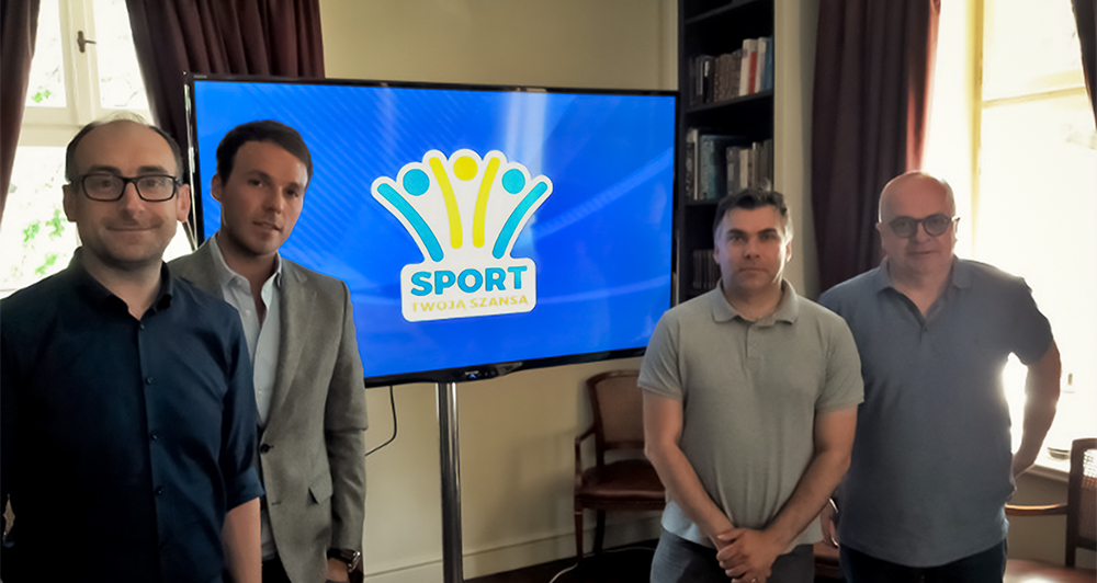 Przedstawiciele Rady Honorowej obok telewizora z logiem Fundacji Sport Twoja Szansa